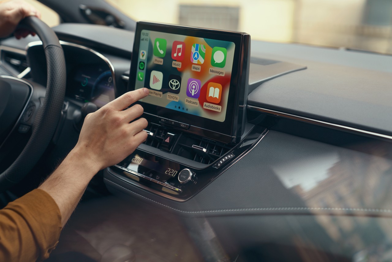 Eine Person in einem Toyota bedient den Touchscreen des Multimedia-Systems. Das Display zeigt die Home-Seite von Apple CarPlay.