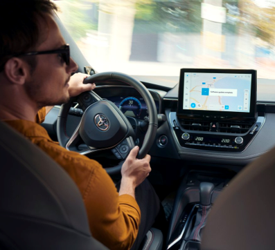 Ein Mann in orangem Pullover steuert seinen Toyota nach rechts. Sein Multimedia-System signalisiert eine Software-Aktualisierung.